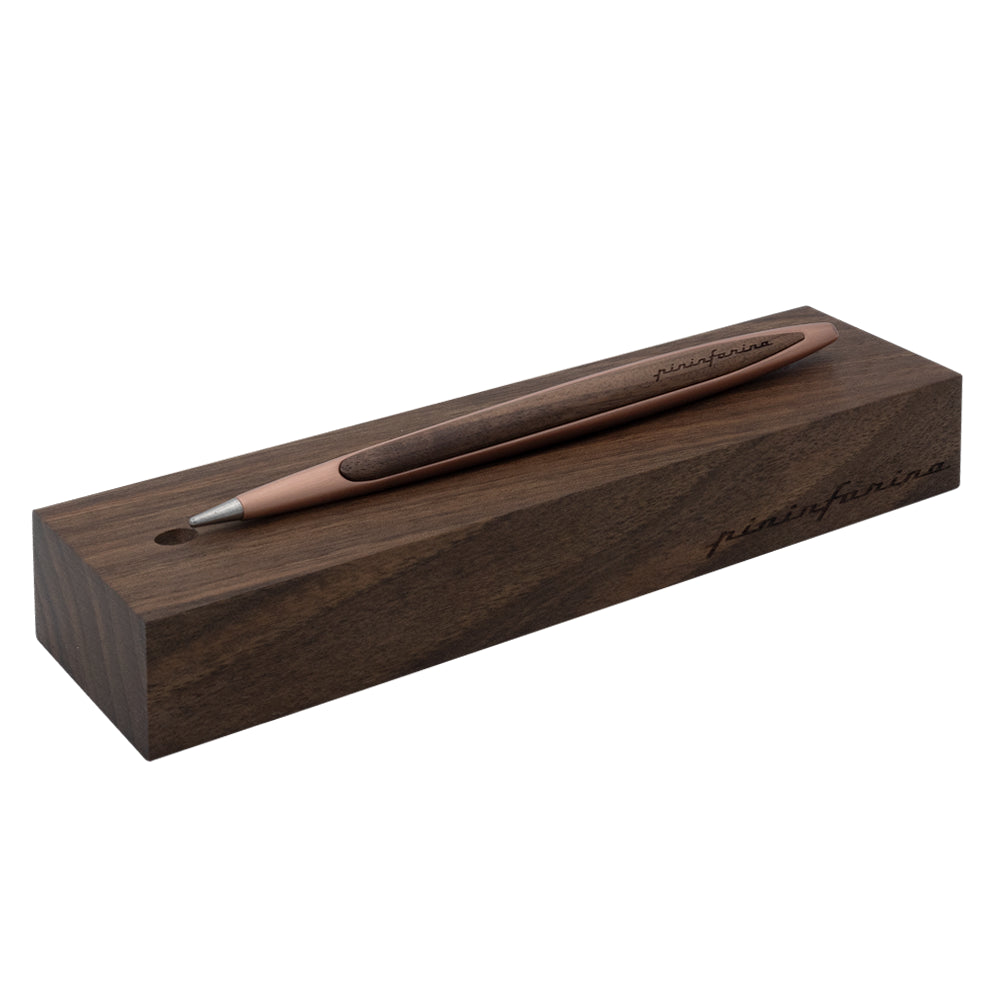 Stylo Forever Pininfarina Cambiano en cuivre posé sur sa base assortie, présentée sur un fond blanc. La base en bois qui fait office aussi d'écrin met en valeur le design moderne et élégant du stylo, soulignant son caractère innovant et durable.